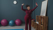 © Krakenimages.com - Woman holds smartphone at arm's length for selfie, touches hair beside exercise balls and wooden crate shelf in gym studio; self care confidence.