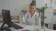 © Krakenimages.com - Woman doctor in white coat with stethoscope and clipboard raises hands in celebratory cheer while seated at desk in a pediatric clinic building; joy achievement.