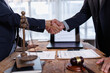 © David - Two people in suits shaking hands at a desk, a legal agreement symbolizing partnership, collaboration, and a successful transaction, surrounded by books, scales of justice, and a gavel