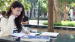 © blueringmedia - Young Thai University Student Studying with Laptop and Notebook Outdoors