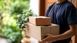 © Bussakon - A person holding two cardboard boxes outdoors near greenery and a wooden door  suggesting delivery or moving