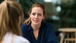 © Thares2020 - A woman with red hair tied back listens attentively while seated across from another person during a conversation