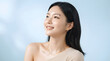 © PTC - Radiant East Asian woman with glowing skin smiling brightly against a soft blue studio background for skincare and beauty concept