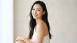 © PTC - Smiling elegant Asian woman with long dark hair wearing a white top in a soft minimalist indoor setting