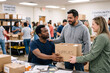 © Thomas Parker - Diverse gay couple volunteers exchange supplies at a busy community outreach center, showing mutual aid.