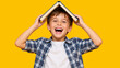 © Vyatcheslav - Laughing little boy holding an open book on his head like a roof. Happy child playing against a yellow background. Education and fun learning concept