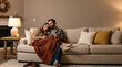 © Yoiduct - Happy Young Couple Relaxing on Sofa at Home Under Blanket with Drinks in Cozy Living Room
