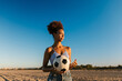 © Ezequiel Gimenez/Stocksy - Young woman holding soccer ball on beach at sunset