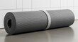 © Platon - Rolled up gray yoga mat secured with a strap lying on a smooth floor.