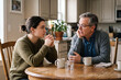 © Thomas Parker - Young adult sharing personal truth with father during emotional kitchen table conversation.