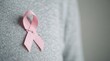 © velikiyzayats - Pink ribbon breast cancer awareness symbol pinned to grey sweater for health campaign and medical support concept
