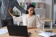 © Prostock-studio - Worried Hispanic Woman Sitting At Desk In Office, Facing Away And Looking Concerned As Man Reaches Out Towards Her. Tense Interaction Depicting Uncomfortable Situation In Work Environment.