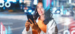 © Prostock-studio - Smiling Young Woman Using Smartphone While Standing Outdoors At Night In City, Engaged With Digital Technology And Embracing Modern Connection In Urban Environment. Inspired Lifestyle Concept.