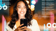 © Prostock-studio - Smiling Young Woman With Long Dark Hair Using Smartphone, Sitting Outdoors At Night In Urban Setting Surrounded By Lights. Positive Emotion Conveyed In A Tech-driven Environment. Technology Concept.