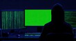 © Danil - Silhouette in hooded jacket faces three screens, two with code, one green
