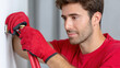 ©  VladaToday - Installer connecting flexible hose to wall-mounted water heater with protective gloves during heater hookup, home repair demonstration for service manuals, contractor listings maintenance instructions
