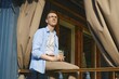 © Aleksei Isachenko/imageBROKER - Middle-aged man sits on balcony in casual clothes holding drink. He looks out towards green trees and blue sky. Sunlight shines on him while he enjoys moment of relaxation in afternoon in wooden cabin