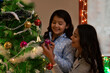 © IndiaPix - Mother and daughter decorating Christmas tree together at home.