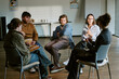 © AnnaStills - Diverse young adults sitting in circle, sharing feelings during group therapy session, supporting mental health recovery. Useful for counseling, addiction treatment, wellness marketing