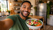 © Vyatcheslav - Smiling Black man holding a fresh salad bowl in the kitchen. Happy young male taking a selfie with a healthy meal. Nutrition and wellness concept