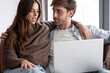 © luciano - Young couple relaxing together on a sofa, looking at a laptop screen and having a conversation at home, enjoying shared digital content and connection