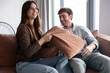 © luciano - Young couple enjoying an energetic pillow fight on their living room couch, sharing a moment of joy, playfulness, and authentic connection at home