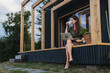 © Halfpoint - Young woman sitting on tiny house patio, working on laptop.