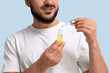© Pixel-Shot - Young man with bottle of vitamin E serum on blue background, closeup