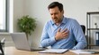 © Artyom - Man in an office clutching his chest in pain, grimacing at a laptop and paperwork, suggesting a sudden medical emergency or heart-related episode