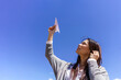 © Javier Zayaz - Young Asian woman launching paper airplane towards clear blue sky, expressing future aspirations and dreams