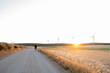 © Nazareno - Person running on rural road at sunset with wind turbines