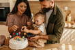© La Famiglia - Family decorating birthday cake with blueberries in kitchen