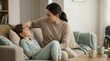© Xenia - Mother checking her sick daughter's forehead with her hand for fever symptoms. Concerned parent caring for an unwell child resting on the sofa