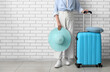 © Pixel-Shot - Woman in casual attire holding a wide-brimmed hat and a blue suitcase, ready for travel or vacation