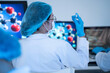 © winnievinzence - Back view of female scientist raising glass slide sample to examine clinical data in front of computer monitor showing molecule model inside medical laboratory