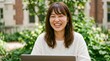 © Majistd - Woman Smiling While Using Laptop Outdoors.