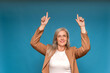 © Renata Hamuda - Smiling mature businesswoman in blazer pointing upward with both hands on blue background