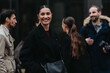 © qunica.com - Smiling businesswoman stands in the foreground with colleagues behind her. A group of professionals chat casually on a city street.