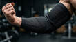© Jaman - Muscular arm wearing black compression elbow sleeve in gym for workout