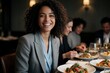 © Pete - Smiling woman with curly hair enjoys meal with colleagues at table. Diverse group shares food and conversation. Pro people dine in elegant restaurant setting with wine. Happy social gathering.
