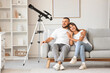 © Pixel-Shot - Young couple with telescope hugging on sofa at home