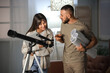 © Pixel-Shot - Young couple with laptop and telescope in room at night