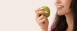 © Pixel-Shot - Young woman with healthy white teeth smiling while holding a fresh green apple, promoting healthy eating and dental care