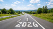 © Mirivox - Open road with year 2026 painted on asphalt, leading through lush green landscape under a blue sky, symbolizing journey and future.
