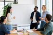 © Olena Apetroaiei - Coworkers laugh together around a blank whiteboard in a sunlit meeting room, capturing bright, collaborative team connection.