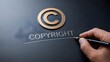 © Picart  - Hand holding pen underlining engraved copyright text with golden symbol on dark surface representing intellectual property rights registration