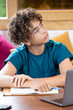 © NataSao - Portrait of a thoughtful teenage boy taking a break while studying at home with a laptop and notebook. Student looking away with a reflective, curious expression during an online lesson