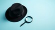 © PhanDesigns - Minimalist investigation concept featuring a black fedora and magnifying glass against a blue backdrop.