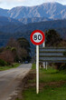 © Zenstratus - An 80 km/h speed limit sign stands along a quiet, scenic rural road in the South Island of New Zealand, framed by beautiful mountain peaks.