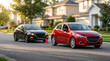 © Mariya Sorvacheva - Towing a black sedan with a flexible hitch attached to a red hatchback on a suburban street lined with houses and trees during golden hour